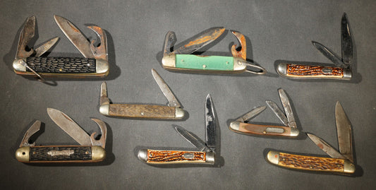 Grouping of Seven Vintage Folding Pocket Knives Including Multi-Tool Camp Knives, Stockman, and Trapper Styles with Bone, Jigged, and Composite Handles
