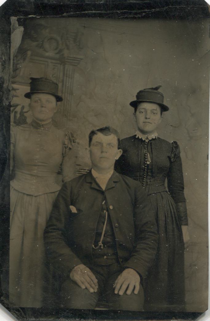 Tintype Photograph of Two Women in Flat Hats Standing Beside a Seated Young Man